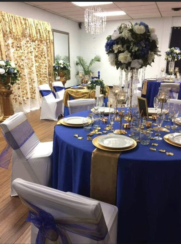 A table prepared with blue and gold linens, flowers, and place settings.