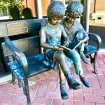 Bronze statue of two kids on a bench reading