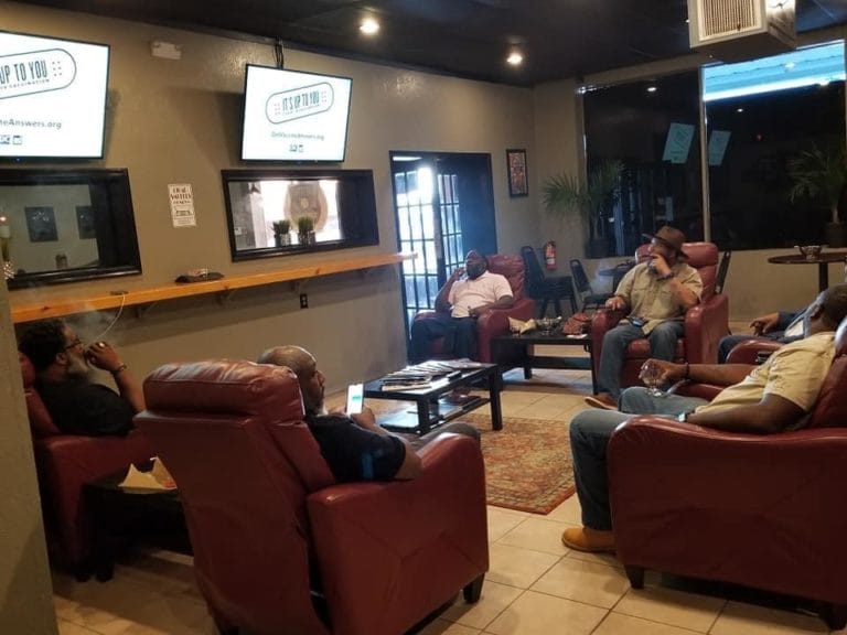 Patrons smoke cigars in red recliner chairs within Flat Street Cigar Lounge