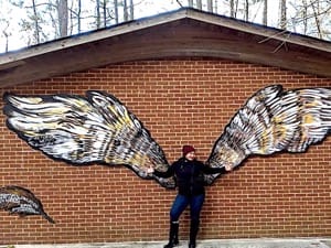 A women poses in front of the Portsmouth Public Art Wings entitled "Owl Wings"
