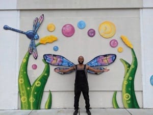 A man poses in front of t he Portsmouth Public Art Wings entitled "Flitting Dragonfly"