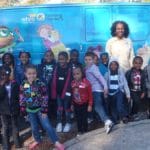 Ms Martha Reads stands in front of a van with children