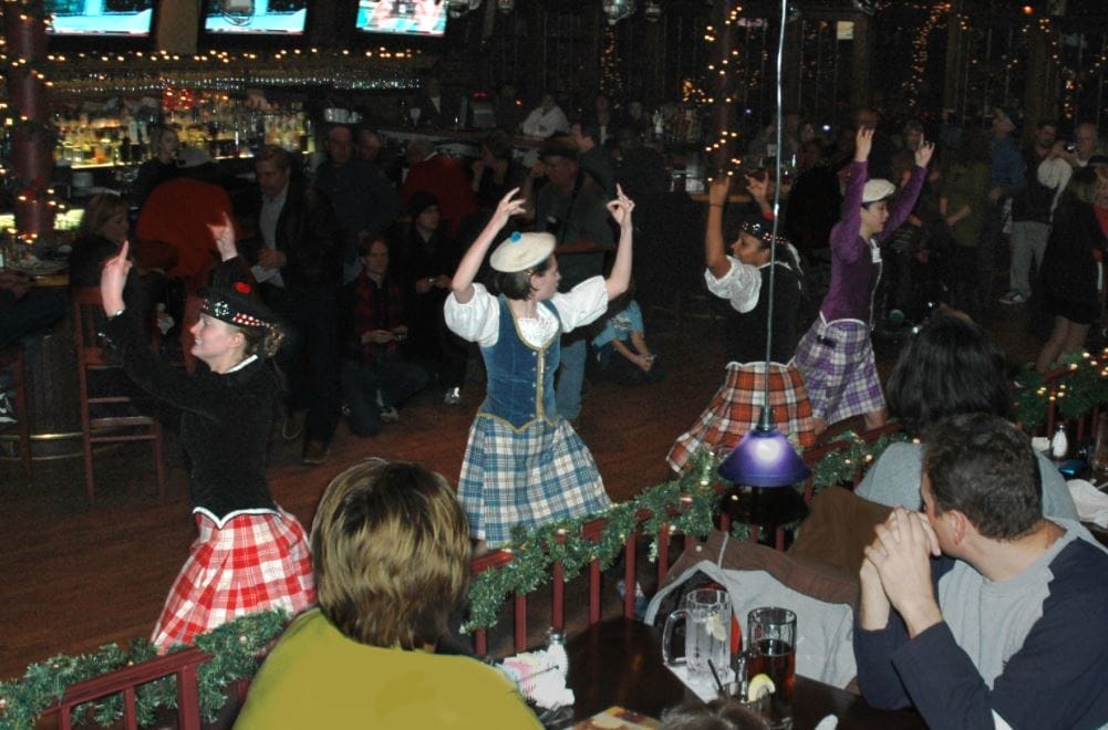 Four women dance in plaid skirts in a restaurant
