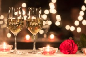 Two glasses of wine and a rose on a candlelit table
