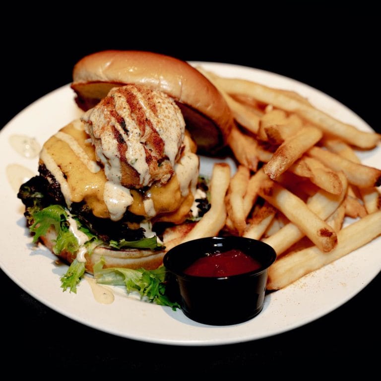 A cheeseburger topped with a crab cake and a side of fries. A cheeseburger topped with a crab cake and a side of fries.